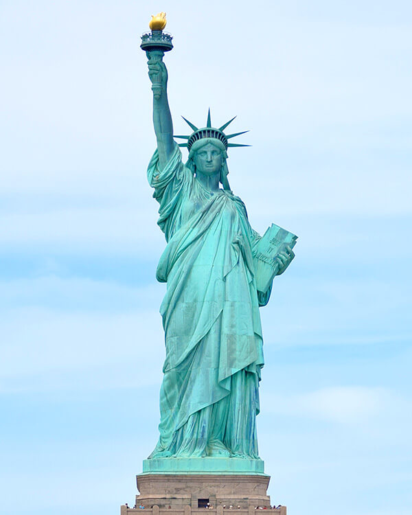 Large statue of woman holding a book in her left hand and a torch in her right hand.