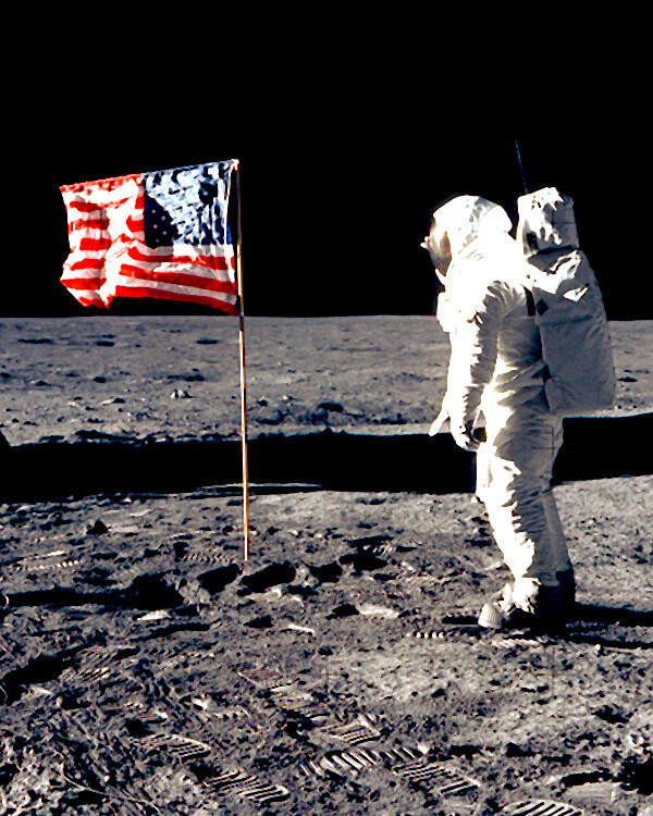 Astronaut standing next to American flag while standing on the moon.